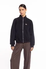 Campera negra de cuello alto con cierre frontal metálico completo, bolsillos laterales y logo bordado en el pecho.