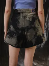 Short de tiro alto confeccionado en denim con lavado Overo de efecto irregular en negro y gris. Presenta una silueta corta y levemente evasé con pierna amplia, ruedo curvo y recortes delanteros Rayo definidos mediante pespuntes visibles, además de pretina estructurada con cierre frontal y botón metálico.