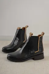 Botas tipo Chelsea de cuero negro, con paneles laterales elásticos y detalle de textura grabada en el talón. Presentan un borde en color beige y tiradores en la parte superior.