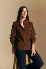 Camisa de pana color crema con cuello camisero con volados, cierre frontal de botones y mangas largas con puños abotonados. Presenta un bolsillo aplicado en el pecho y una silueta relajada.
