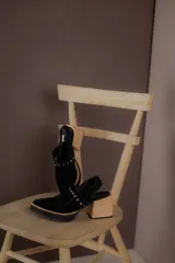 Zapatos tipo zueco de gamuza negra con punta fina y tira sobre el empeine decorada con tachas metálicas plateadas. Posee taco cuadrado de madera y suela con plataforma.