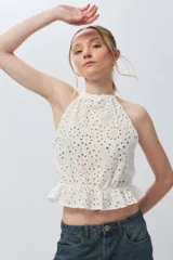 Top blanco sin mangas con cuello halter, bordado con calados y elástico con volado en la cintura.