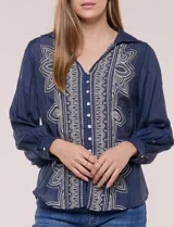 Camisa de estilo boho, color verde, con cuello camisero, escote en V y botonadura frontal con botones perlados. Cuenta con una pechera con bordados geométricos y florales a contraste, mangas largas abullonadas con puños abotonados y delicados bordados dispersos.