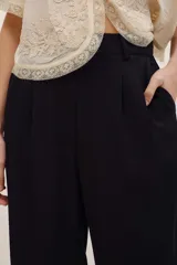 Pantalón negro de vestir de corte ancho y relajado, con cintura alta y detalles sutiles en el diseño.