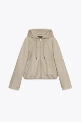 Chaqueta bomber con capucha ajustable mediante cordones, confeccionada en tejido efecto ante. Presenta cierre frontal con cremallera, bolsillos laterales y bajo con elástico interior para un ajuste ceñido.