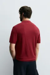 Polo de manga corta color bordó, con cuello solapa y abertura frontal. Tejido de punto con estructura acanalada.