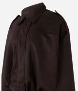 Campera bomber de gamuza sintética color marrón oscuro, con cuello clásico, cierre frontal, hombros caídos y puños ajustados. Presenta un diseño holgado con textura aterciopelada.