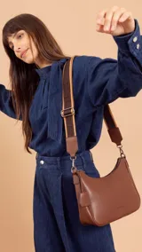 Bandolera de cuero sintético color marrón, con cierre trasero y división interna. Incluye correa de galón ajustable y un pequeño charm colgante.