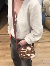 Bandolera de cuero marrón con panel frontal de piel sintética con estampado animal en tonos verde oliva y marrón. Tiene correa larga regulable, cierre superior con cremallera y forro interior.