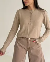 Sweater de punto color beige, con cuello redondo y cierre frontal parcial con botones. Presenta mangas largas con puños acampanados con detalle de volados.