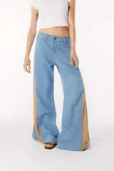 Pantalón de jean azul oscuro de pierna ancha y tiro medio, con paneles laterales en contraste de color marrón. Presenta costuras pespunteadas en tono tostado y terminación desmechada en el bajo.