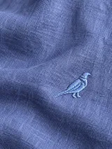 Camisa de lino color blanco, manga larga, con cuello corto clásico y bordado de un ave oscura en el pecho.