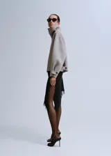 Chaqueta gris de diseño corto y holgado, con cuello alto envolvente, mangas anchas y puños ajustables con tiras y botones. Cuenta con bolsillos laterales y cierre frontal oculto.