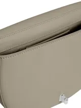 Cartera cruzada Calvin Klein de color beige claro, con forma de media luna o silla de montar. Presenta un logo metálico plateado con las iniciales 'CK' en el frente y una correa ajustable del mismo material.