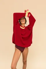 Buzo de punto oversize color rojo, con cuello alto y puños con terminaciones en volados. Presenta detalles en contraste color amarillo en el cuello y los puños, con un tejido de acabado ligeramente brillante.