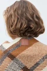 Ruana de tejido grueso con diseño de cuadros en tonos beige, marrón y gris, con terminación de flecos en los bordes.
