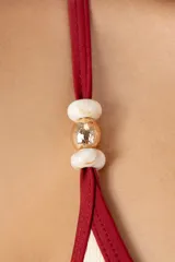 Top de bikini triangular color marfil con ribete rojo oscuro, tirantes finos con anillos dorados y faja inferior.