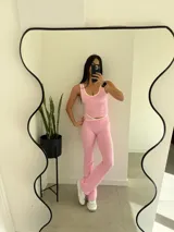 Conjunto deportivo de dos piezas en color rosado con detalles en blanco. Incluye una musculosa de escote redondo y un pantalón tipo flare de tiro medio con detalle cruzado en la cintura.