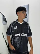 Camiseta de estilo deportivo con cuello en V, manga corta y diseño estampado con motivos de telarañas y arañas. Presenta el número 88 y la inscripción 'SOA CLUB' en el frente.