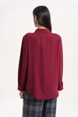 Camisa clásica de manga larga en color bordó, confeccionada en tela ligera con caída fluida, cuello camisero y cierre frontal con botones al tono.