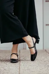 Zapatos estilo Mary Jane de cuero negro con acabado brillante, punta redondeada, tira con hebilla ajustable sobre el empeine y taco cuadrado forrado de 6 cm.