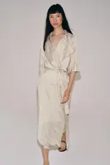 Vestido midi de Zara Woman Collection color beige, con cuello solapa, mangas por debajo del codo y diseño cruzado. Confeccionado en tejido plisado con brillo satinado, incluye un cinturón ajustable del mismo género con lazada en la cintura.