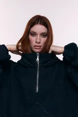 Canguro oversize confeccionado en denim negro 100% algodón, con capucha, cuello alto con cierre metálico frontal, bolsillo frontal tipo canguro y puños con elástico.