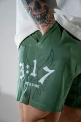 Short deportivo de color verde militar, con diseño estampado en blanco que incluye números y alas. Presenta aberturas laterales en el ruedo para mayor movilidad y bolsillos laterales.