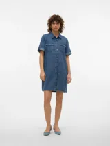 Vestido corto de denim en tono celeste claro, con cuello camisero, cierre frontal con botones metálicos, bolsillos con solapa en el pecho y mangas cortas con vuelta.
