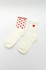 Pack de dos pares de medias blancas tipo crew, una con estampado all-over de corazones rojos y ribetes rojos en el puño, y la otra lisa con un único corazón rojo bordado en el lateral.