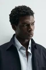 Sobrecamisa de corte relajado confeccionada en tejido de algodón con elasticidad. Presenta cuello solapa, cierre frontal con botones, manga larga con puños abotonados y dos bolsillos plastrón en el pecho.
