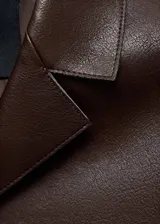 Chaqueta corta de efecto piel en color marrón chocolate, con cuello camisero, cierre frontal con botones y dos bolsillos de parche delanteros.