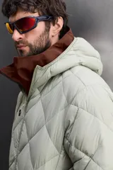 Campera puffer verde oliva acolchada con diseño de rombos, capucha y cierre frontal con cremallera. Incluye bolsillos laterales con cierre. Relleno de plumón y plumas.
