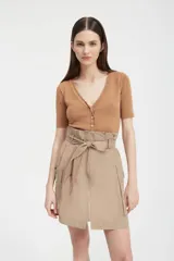 Minifalda color tostado de tejido tecnológico con cierre frontal con cremallera metálica, bolsillos laterales con fuelle y lazo en la cintura.