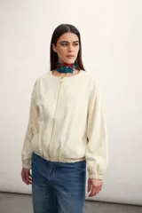 Chaqueta tipo bomber de color beige, con cierre frontal completo, cuello redondo y puños elásticos.