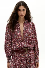 Camisa de lino con estampado floral de margaritas sobre fondo color vino. Presenta cuello camisero clásico, botones frontales de nácar, mangas largas abullonadas y puños con terminación ondulada.