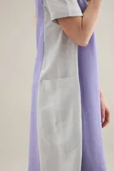 Vestido largo de lino de silueta relajada, con escote redondo, mangas cortas y bolsillos laterales. Cuenta con un diseño bicolor que combina un panel central en color tostado y los laterales y mangas en color blanco.