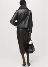 Chaqueta tipo coach de efecto piel en color negro, con diseño oversize, cierre frontal con cremallera, cuello camisero y forro interior de borreguito en color marrón.