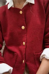 Cardigan de punto color beige con cuello redondo, cierre frontal con botones dorados, bolsillos frontales y terminaciones en crochet. Presenta hombreras internas y diseño de corte recto.