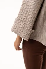 Camisa de textura plisada en color beige, con cuello clásico, cierre frontal de botones y mangas tres cuartos con puños vueltos.