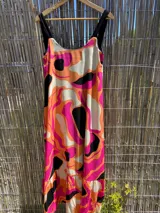 Vestido largo sin mangas, con escote cuadrado y falda con volado en el ruedo. Presenta un estampado abstracto y psicodélico en tonos fucsia, naranja, blanco y negro.