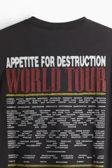 Remera negra de algodón de peso medio, corte holgado (Loose Fit), con cuello redondo. Estampado frontal con el logo de Guns N' Roses, una calavera con una rosa y una cadena, y el texto "Appetite for Destruction 1987-1988".