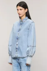 Camisa de denim celeste con calce regular, cuello camisero, cierre frontal con botones metálicos y mangas estilo balloon con puños largos ajustables.