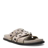 Sandalias planas de mujer de estilo urbano, confeccionadas en material sintético símil gamuza de color beige. Presentan un diseño destalonado con dos tiras anchas en el empeine decoradas con tachas metálicas oscuras. Cuentan con una base plana con plantilla anatómica para mayor comodidad.