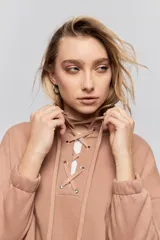 Buzo de calce relajado color tostado, con cuello alto y detalle de cordones entrelazados con ojales metálicos en el frente. Posee bolsillos laterales ocultos y puños y ruedo elastizados.