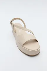 Sandalia negra con plataforma, tiras cruzadas sobre el empeine y pulsera ajustable al tobillo.