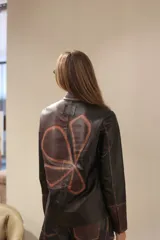 Camisa de cuero con diseño de patchwork en tonos negro y marrón oscuro, con efecto desgastado en las costuras. Presenta cuello camisero, botones frontales y mangas largas.