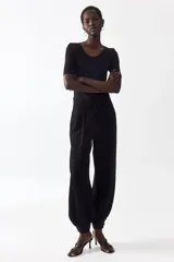 Pantalón de sarga negro de tiro alto con bolsillos laterales discretos y cierre con botón y corchetes ocultos. Presenta diseño de piernas globo con pinzas y puños abotonados con frunces.