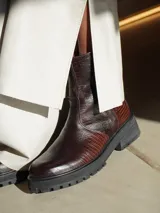 Botas de cuero con textura simil cocodrilo en color marrón, diseño de caña baja con cierre lateral y suela track negra de goma.