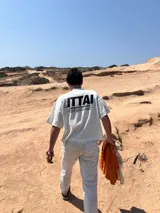 Remera marrón de corte holgado con estampado en la espalda que incluye la palabra "ITTAI" en blanco con líneas rojas y azules, la frase "AN IBIZA PRODUCE" y un texto más pequeño que dice "Ittai Stars Department Gallery - Ibiza Edition. If you're in Ibiza, 112 is not an option.".